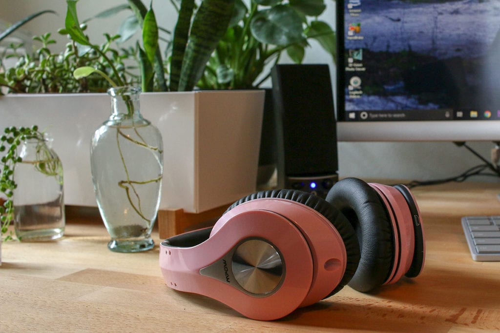 Pink headphones laying on desk next to monitor.