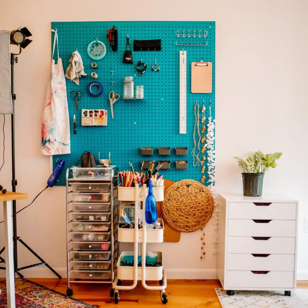 Teal peg board with art supplies and film equipment hanging over two carts full of art supplies.