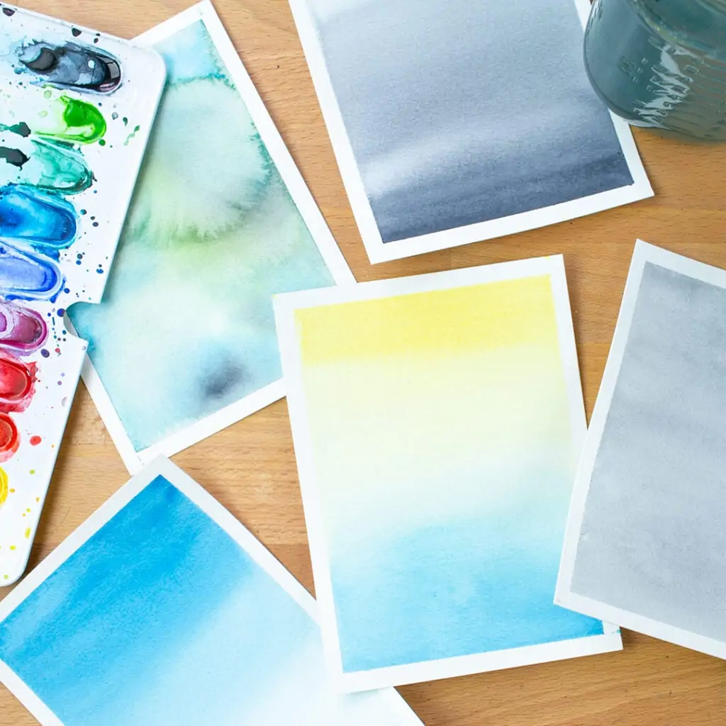 Small pile of pages of different watercolor washes sitting on desk.