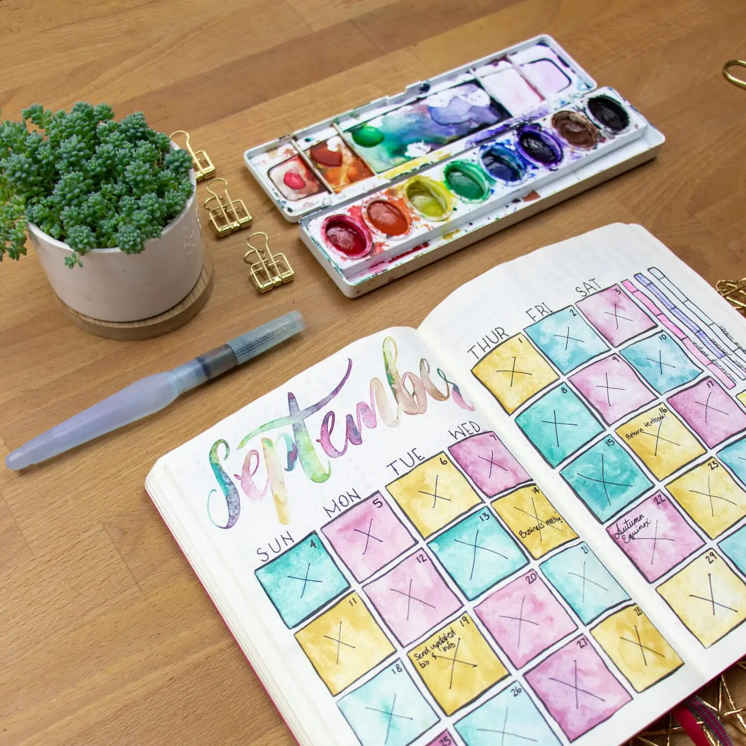Journal open to watercolor calendar with prang watercolor palette open on desk.