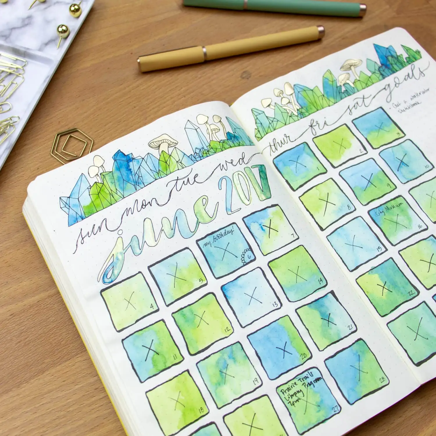 Open journal with watercolored blue and green calendar sitting on desk.